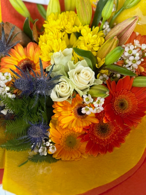 Colorful bouquet of flowers including yellow, orange, red, and white flowers on a yellow background.